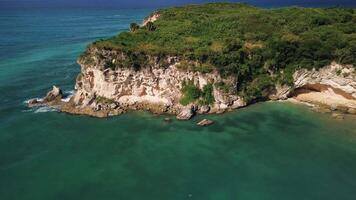 Atrial view of wild tropical coast of the Dominican Republic with rocky cliff and untouched nature.A light breeze rolls onto the shore with turquoise ocean waves.A luxurious landscape for relaxation video