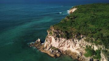 Aerial view of the wild tropical coast of the Dominican Republic with rocky cliff and untouched nature.A light breeze rolls onto shore with turquoise ocean waves.A luxurious landscape for relaxation video
