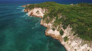 Atrial view of wild tropical coast of the Dominican Republic with rocky cliff and untouched nature.A light breeze rolls onto the shore with turquoise ocean waves.A luxurious landscape for relaxation video