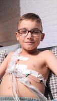 vertical Boy in glasses with sad eyes looks at camera. Medical holter video