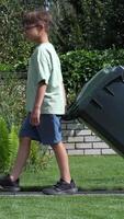 vertical boy rolls out trash can. Boy throws out garbage video