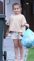 vertical portrait of a little girl with a garbage bag near a trash can video