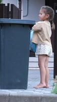 vertical little girl throws a full trash bag of garbage into a trash can. video