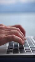 A focused pair of hands types on a laptop, enjoying the calm atmosphere by the water video