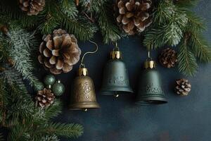 Three Christmas Bells, Pine Cones, and Evergreen Sprigs on a Dark Blue Background photo