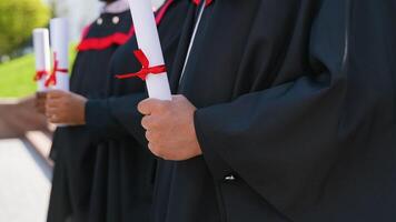 Scrolls of diplomas in the hands of a group of multiracial graduates, close up video