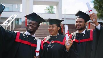Three happy students in graduation gowns making selfie and smiling video