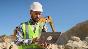 Civil engineer working in quarry use a laptop to check the operation of the yellow excavator video