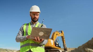 Civil engineer working in quarry use a laptop to check the operation of the yellow excavator video