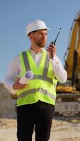 Foreman giving commands to employee in excavator using walkie talkie at construction site. Vertical video