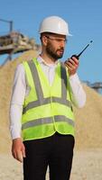 Industrial worker engineer use radio walkie talkie at sand quarry. Vertical video