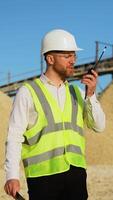 Foreman with laptop instructing workers using walkie talkie radio set at quarry. Vertical video
