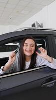 Beautiful woman customer is showing key of her new car, looking at camera and smiling. Vertical video