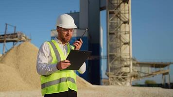 Foreman with clipboard instructing workers using walkie talkie radio set at quarry video