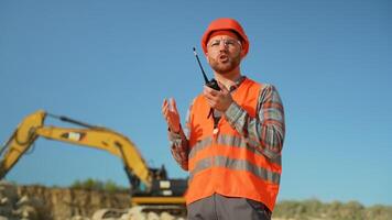 Foreman in uniform giving commands to employee in excavator using walkie talkie at construction site video