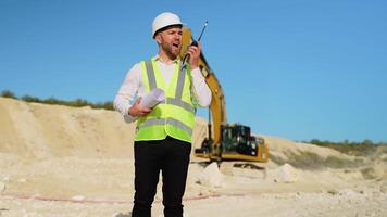 Engineer instructing worker in excavator drill machine using walkie talkie radio set at quarry video