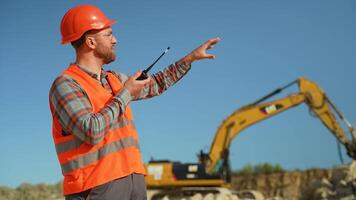 Foreman in uniform giving commands to employee in excavator using walkie talkie at construction site video