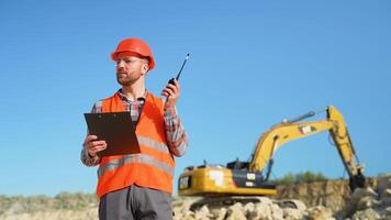 Foreman giving commands to employee in drilling machine using walkie talkie at stone quarry video