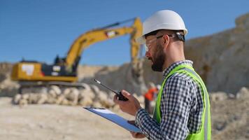 Engineer in uniform giving commands to employee in excavator using walkie talkie at construction site video