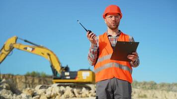 Engineer instructing worker in excavator drill machine using walkie talkie radio set at quarry video