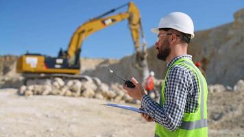 Foreman instructing worker in excavator drill machine using walkie talkie radio set at quarry video