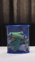 vertical Hand dropping batteries into blue mesh recycling bin on table video