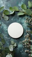 A simple round white plate surrounded by fresh greenery and delicate flowers on a textured surface photo