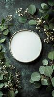 A simple round white plate surrounded by fresh greenery and delicate flowers on a textured surface photo