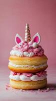 A delightful unicorn cake decorated with pink frosting and whimsical features on a pink background photo