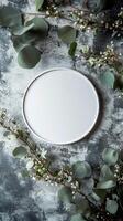 A simple round white plate surrounded by fresh greenery and delicate flowers on a textured surface photo