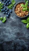 Fresh yogurt topped with granola and basil alongside blueberries on a dark textured surface photo