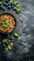 Fresh yogurt topped with granola and basil alongside blueberries on a dark textured surface photo