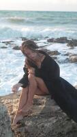 Woman Beach Ocean Waves - A woman sits on a rocky beach, with her hand on her head and looking down, as waves crash behind her. video