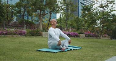Athlete in park on mat takes lotus position for meditation. Correct lotus position provides comfort maximum concentration. Green landscapes park create ideal atmosphere for relaxing in lotus position. video