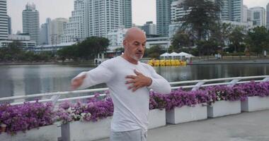 Sporty man in white duffle is warm-up before training on embankment metropolis. Energetic warm-up indicate readiness for loads. Skyscrapers emphasize dynamism warm-up and determination of the athlete. video