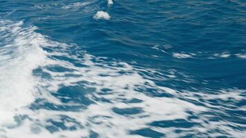 Close-up of waves and splashes with white sea foam forming patterns on surface of deep blue water. Ship trails in blue ocean video