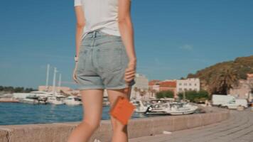Close-up of woman walking in coastal town and holding an orange instant camera in retro style. Summer travel concept. Equipment for capturing moments video