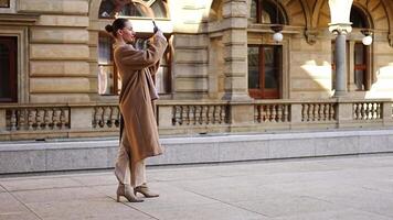 Young beautiful woman wearing coat making selfie with smartphone in the city centre of Prague, Europe. High quality 4k footage video