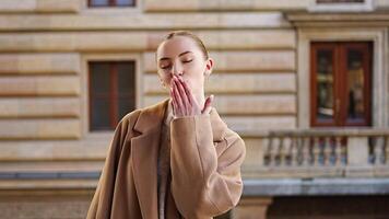 Portrait of a young woman blowing a kiss to the camera and wearing a coat in the center of Prague, Europe. High quality 4k footage video