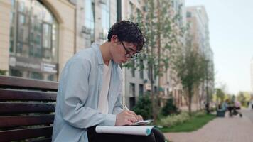 Student diligently taking notes while seated on a park bench video