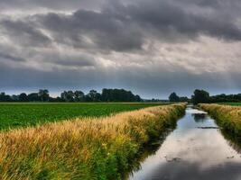 A canal in the middle of a field with dark clouds photo