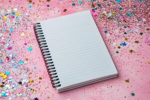 Blank notebook on pink background surrounded by colorful star confetti photo