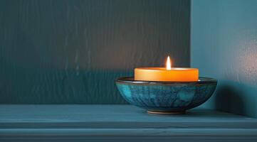 A Single Burning Candle in a Blue Bowl on a Textured Blue Surface photo