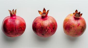 Three Ripe Pomegranates Arranged in a Row on a White Background photo