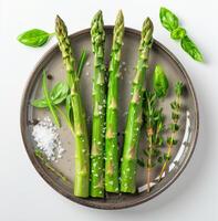 Four Green Asparagus Spears With Salt and Herbs on a Grey Plate photo