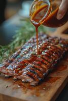 Delicious barbecue ribs being glazed with sauce on a wooden cutting board photo