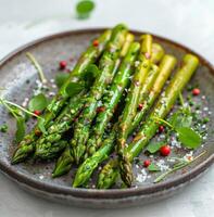 Four Green Asparagus Spears With Salt and Herbs on a Grey Plate photo