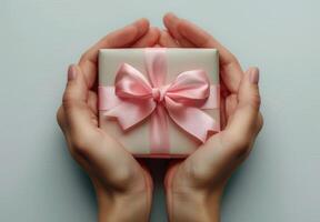 Close Up Of Two Hands Holding A Pink Gift Box With A Bow photo