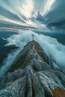 Dramatic mountain peak with a cross, surrounded by clouds and an expansive sky at sunrise photo