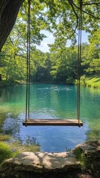 A serene swing overlooking a clear, tranquil lake surrounded by lush greenery on a sunny day photo